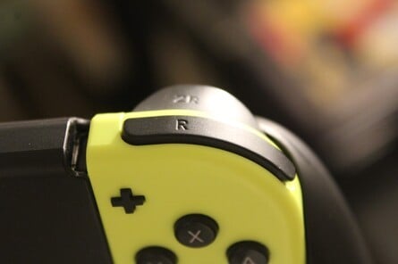 The 'L' and 'R' buttons on a Pro Controller and Neon Yellow right Joy-Con respectively. Note the small pairing button next to the USB-C port on the Pro Controller.