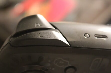 The 'L' and 'R' buttons on a Pro Controller and Neon Yellow right Joy-Con respectively. Note the small pairing button next to the USB-C port on the Pro Controller.